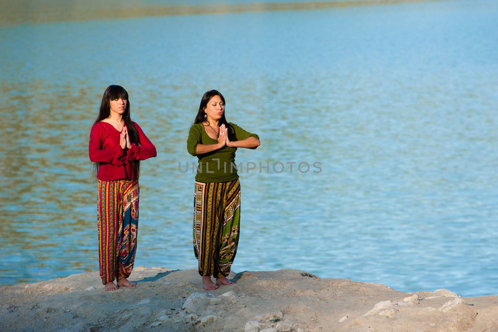 Mother and daughter enjoying yoga exercises on the shores of a lake