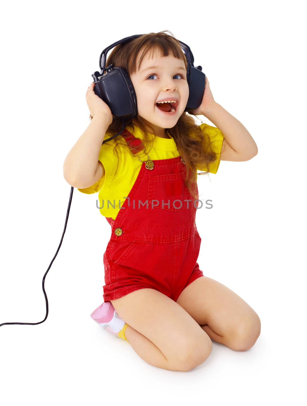 A little girl sitting on a white background with large earpieces