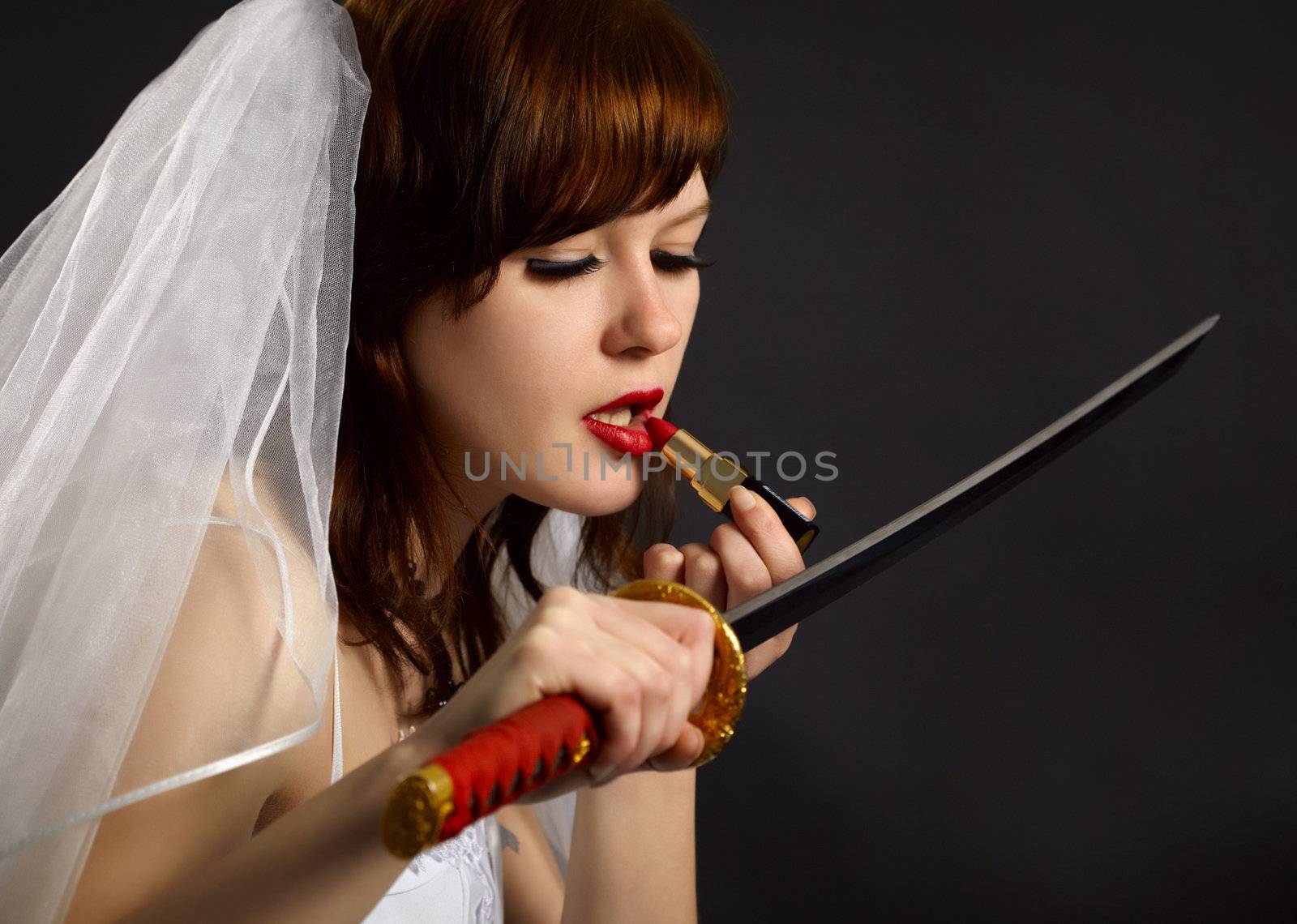 Girl lipstick looking at the blade of the sword as a mirror on dark background