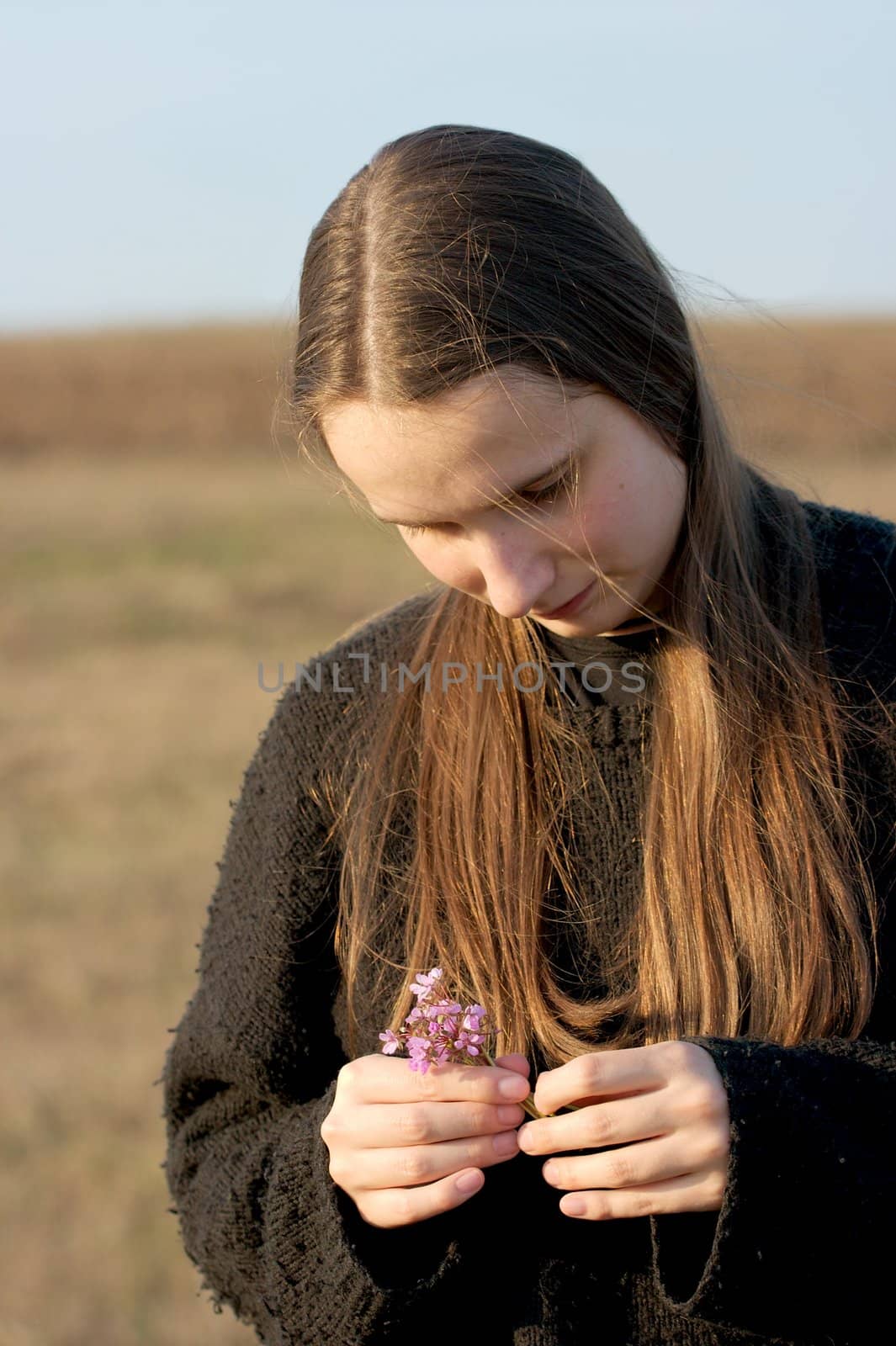 Girl standing in a field holding a flower