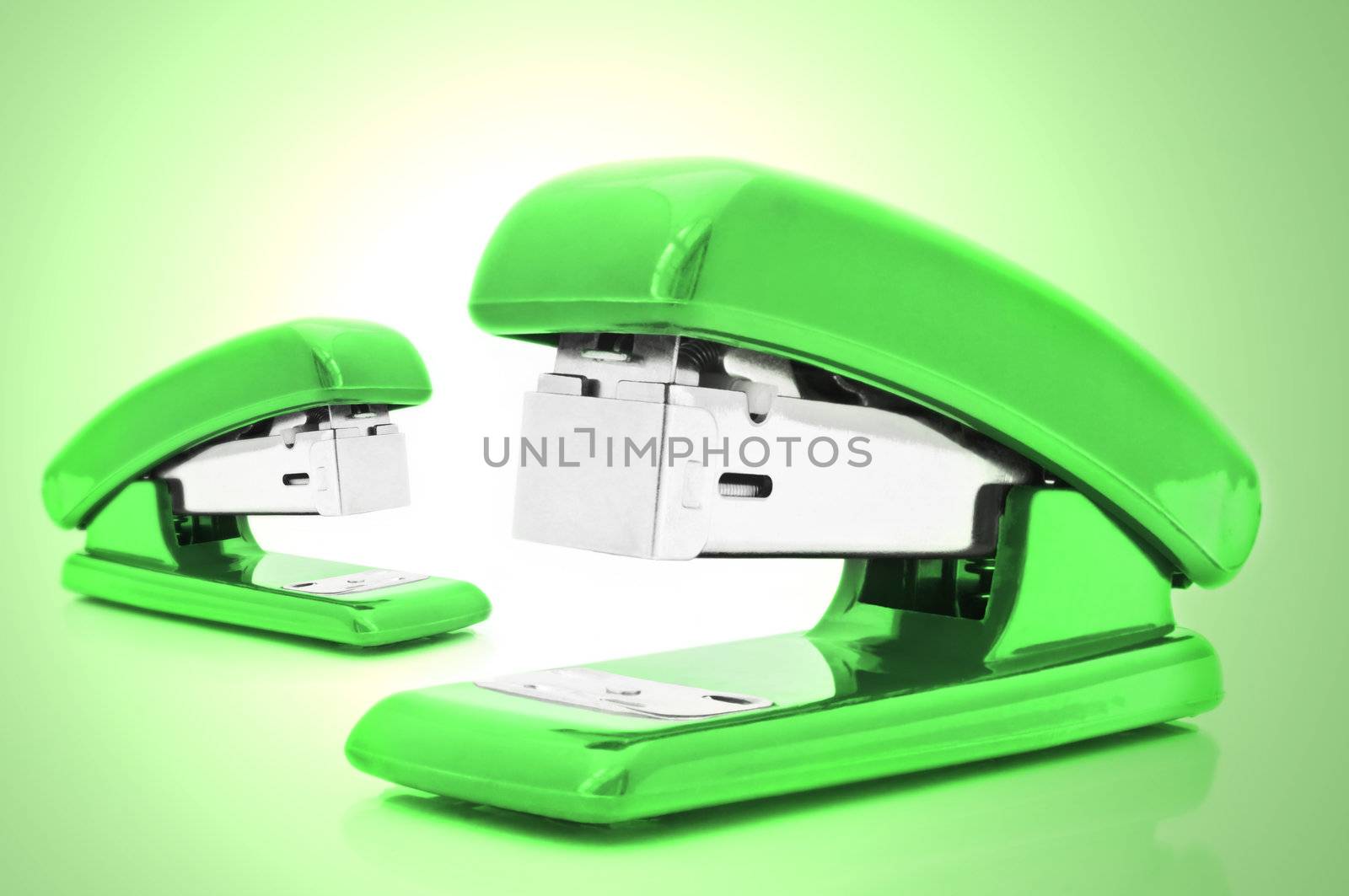 Close up of two green office staplers isolated over pale green light effect