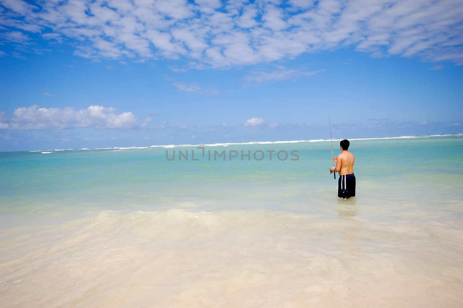 Man is fishing on An exotic beach with white sand, the sky is blue with clouds. Dominican Republic, Punta Cana.