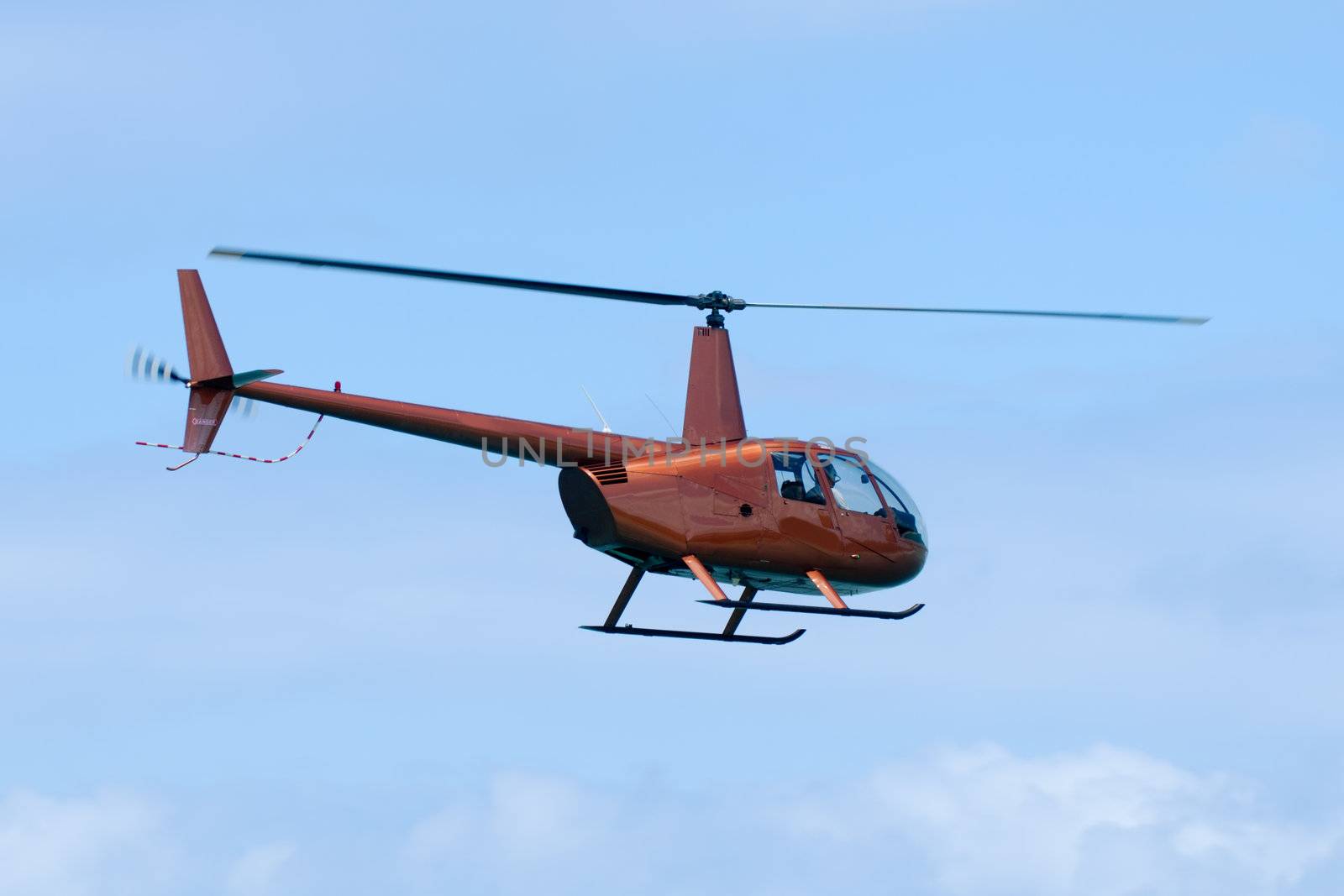 Orange helicopter is flying in blue sky