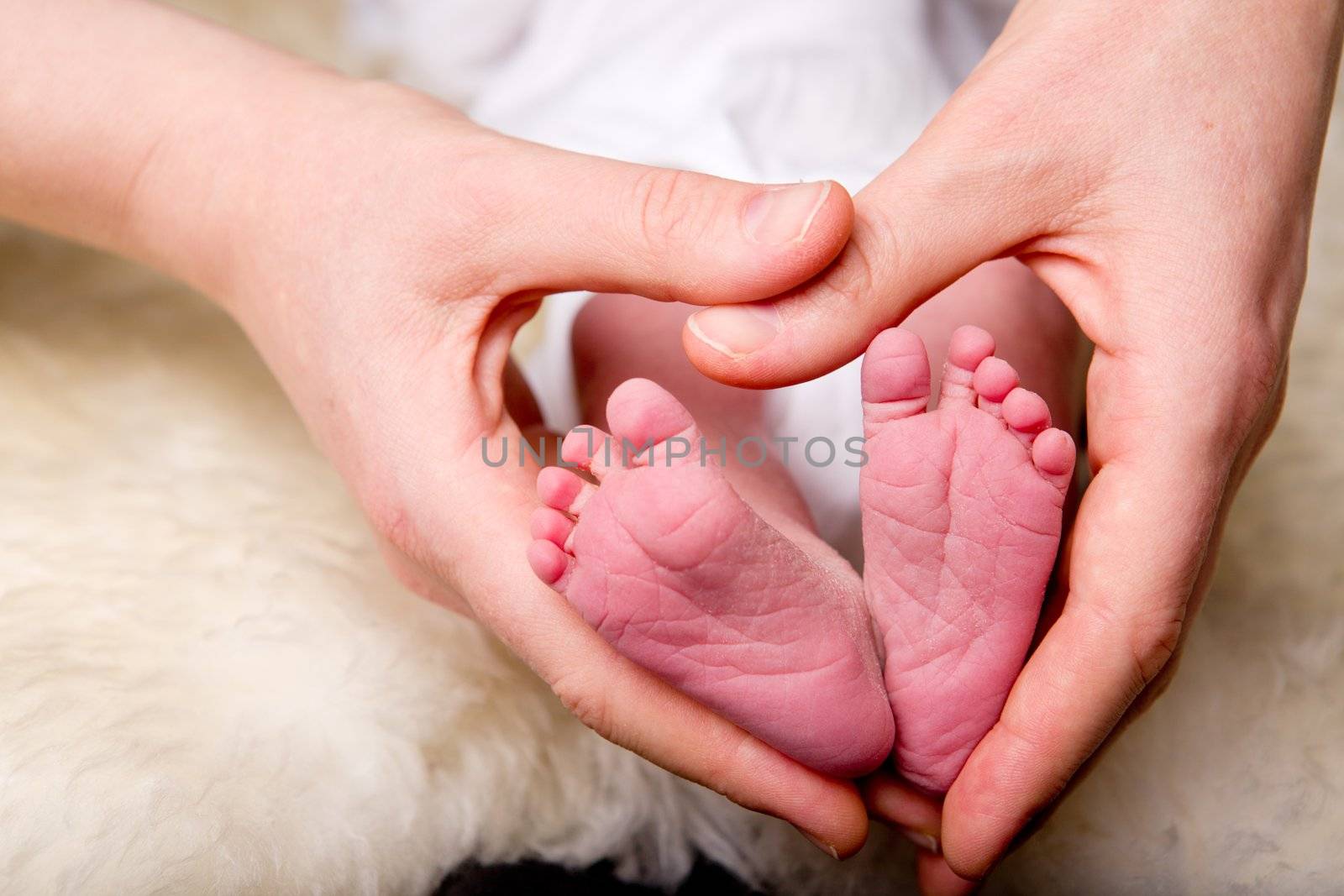 A mother's hands in the shape of a heart around a newborn baby's feet