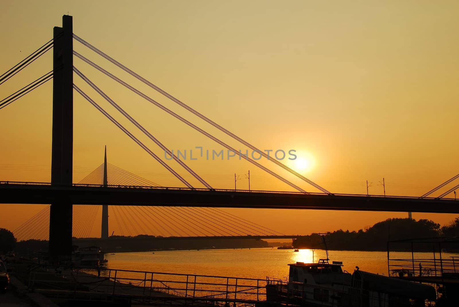 suspension bridges silhouettes on Sava river over orange sunset  in Belgrade, Serbia