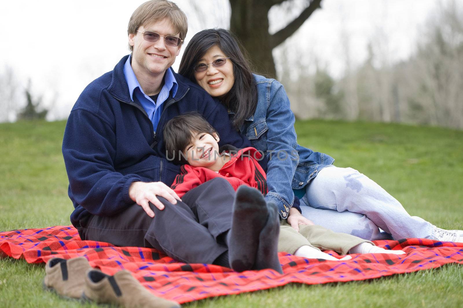 Father and mother sitting at park with disabled son, interracial family