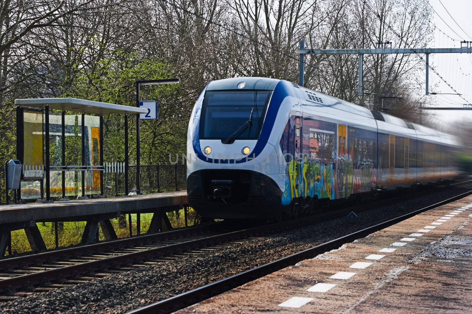 Suburb train passing by at small station by Colette