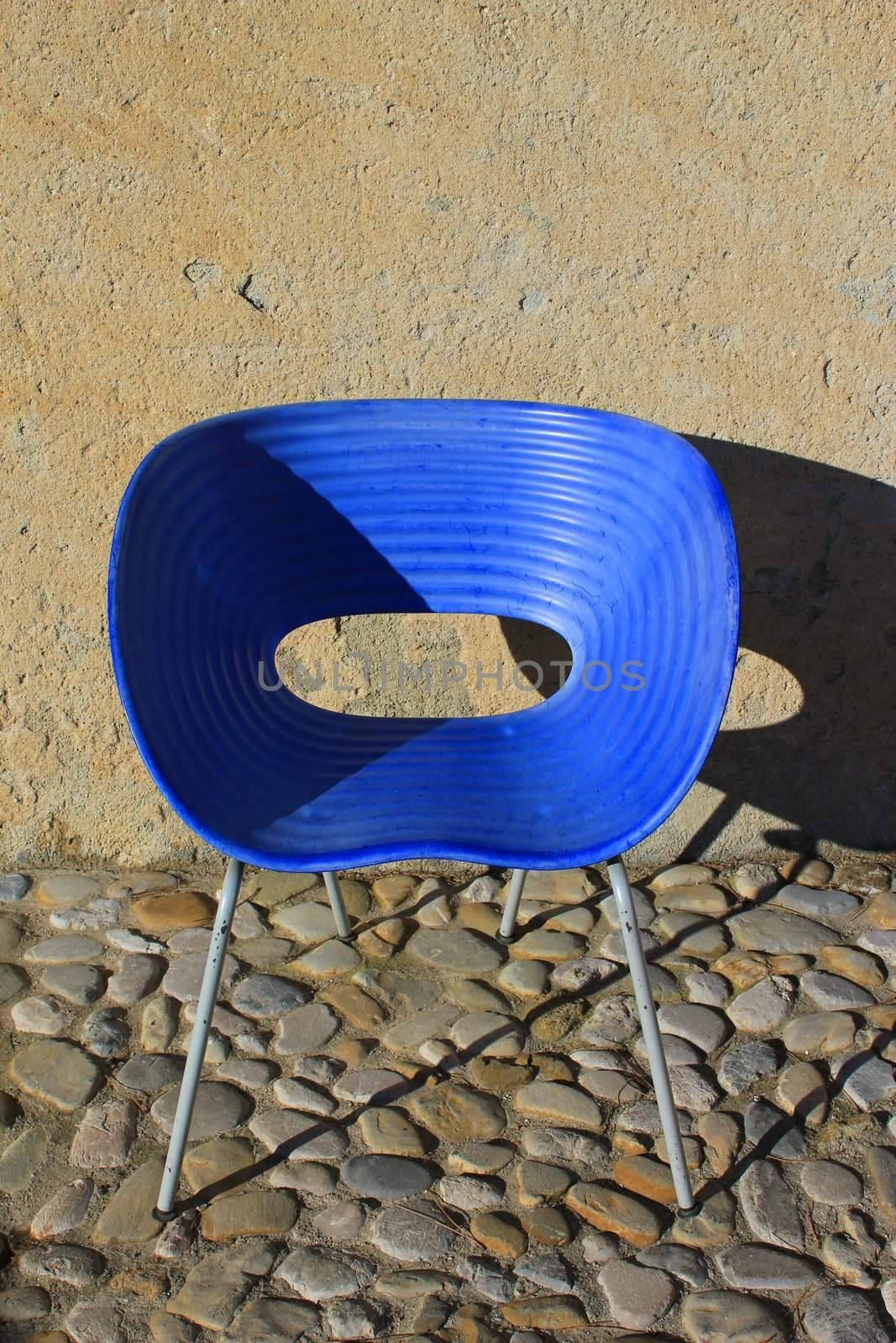 Modern style blue chaire in front of an outside wall and on a ground made of stones