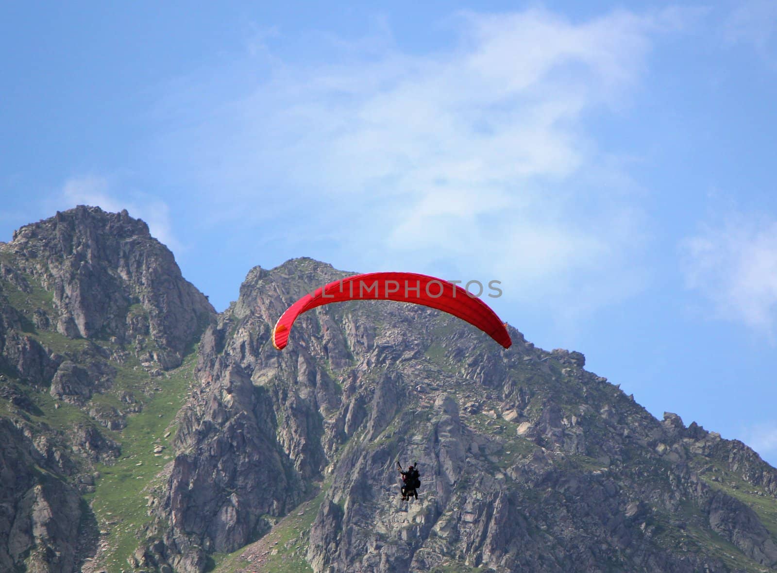 Red paraglider flying in the sky next to a rocky mountain