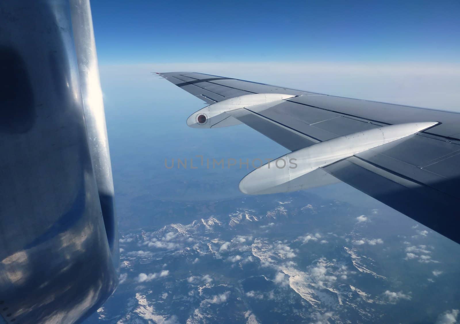 Flying plane wing and motor in a deep blue sky and upon mountains