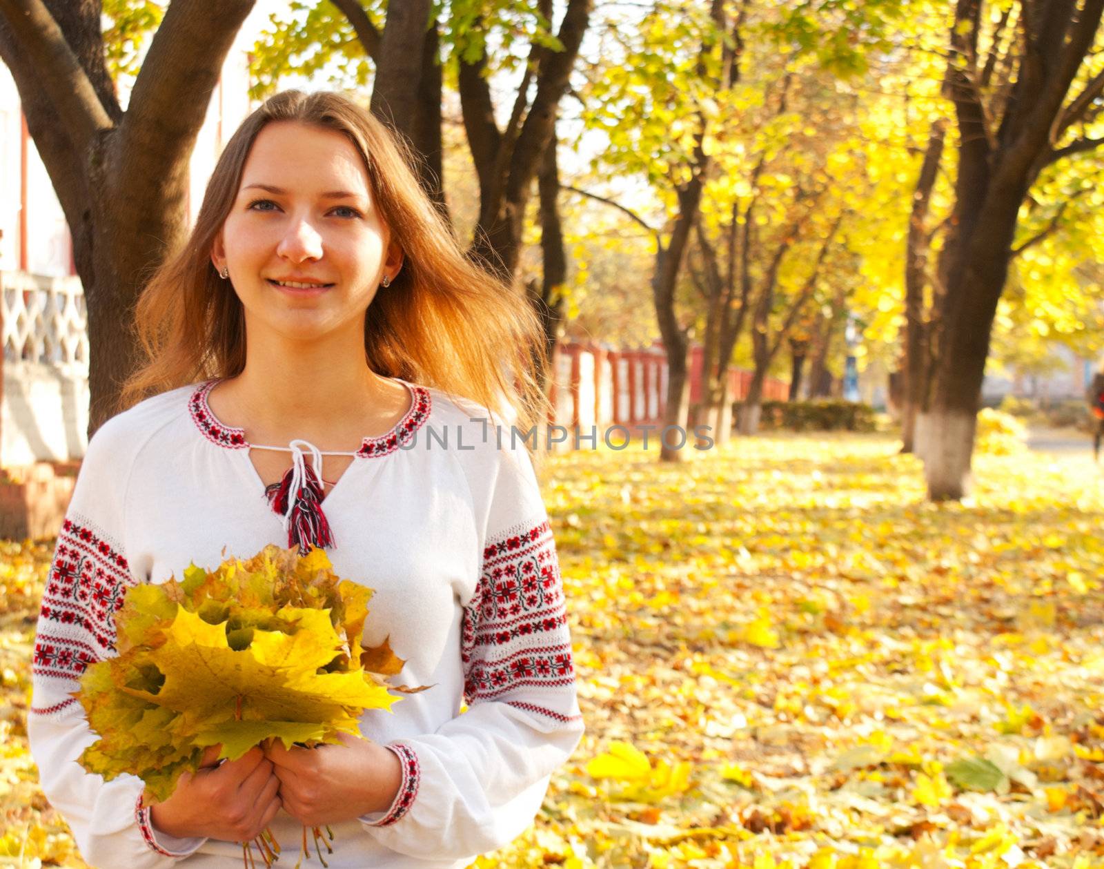 Young lady sitting in a park at fall time by AndreyKr