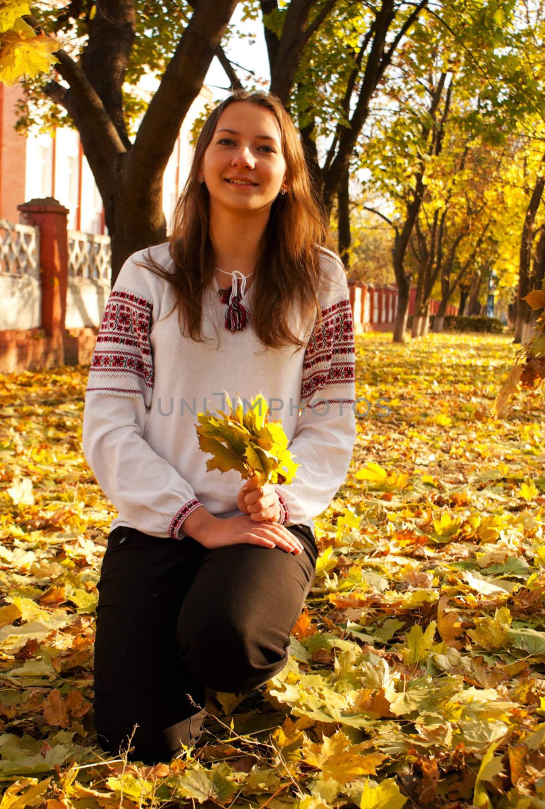Young lady sitting in a park at fall time by AndreyKr