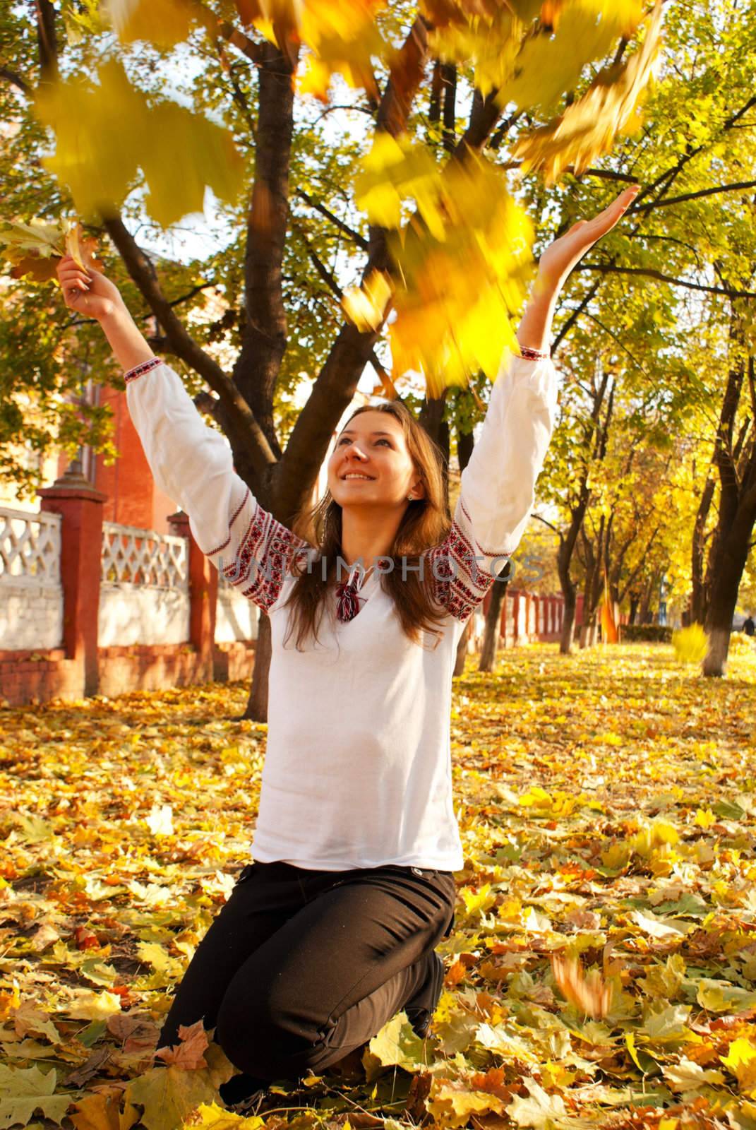 Young lady playing with leaves in a park at fall time