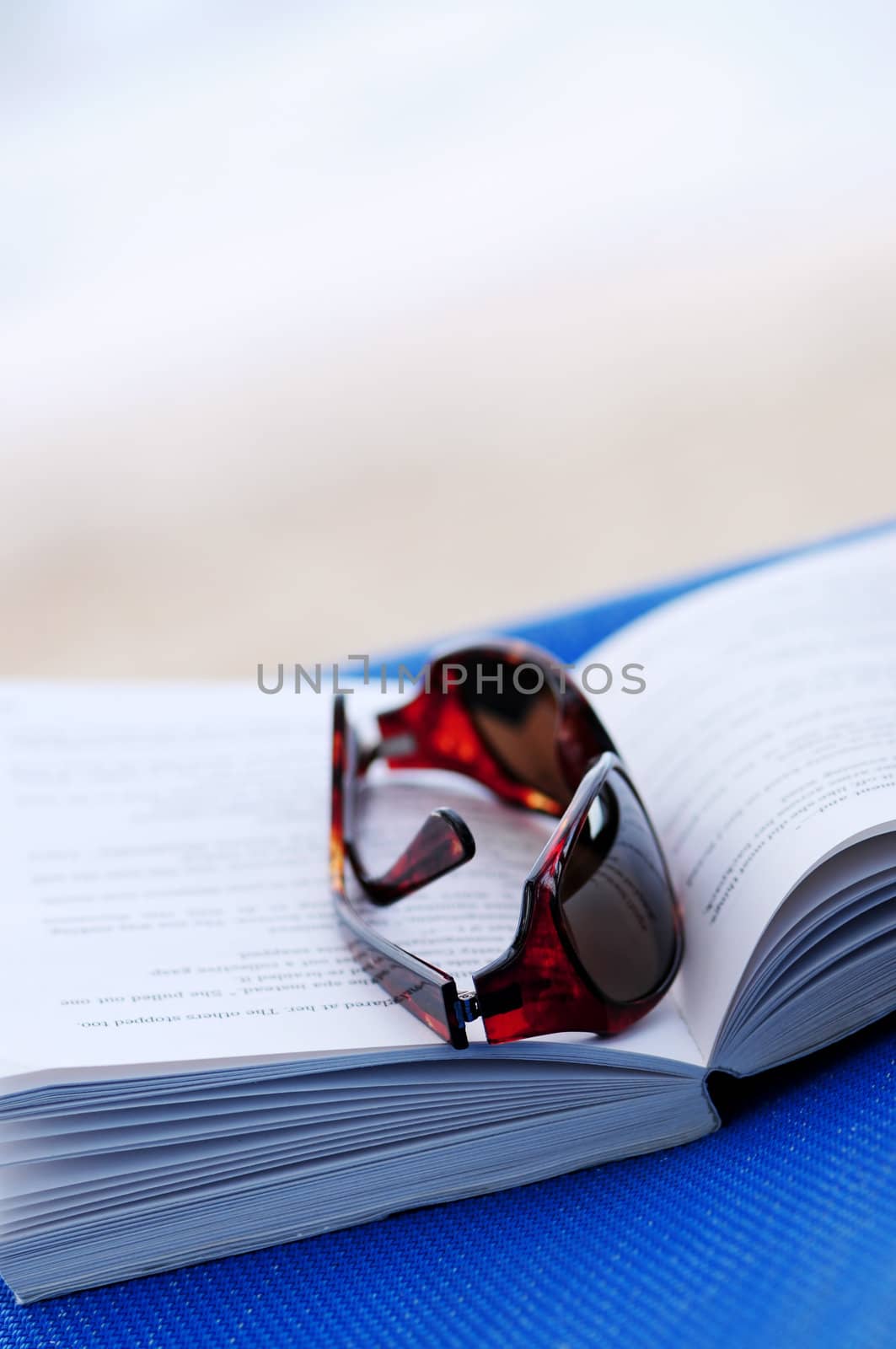 Sunglasses and open book on beach chair - summer vacation concept