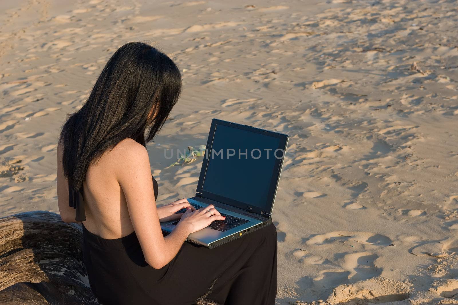 Attractive woman working on a laptop with the beach as background