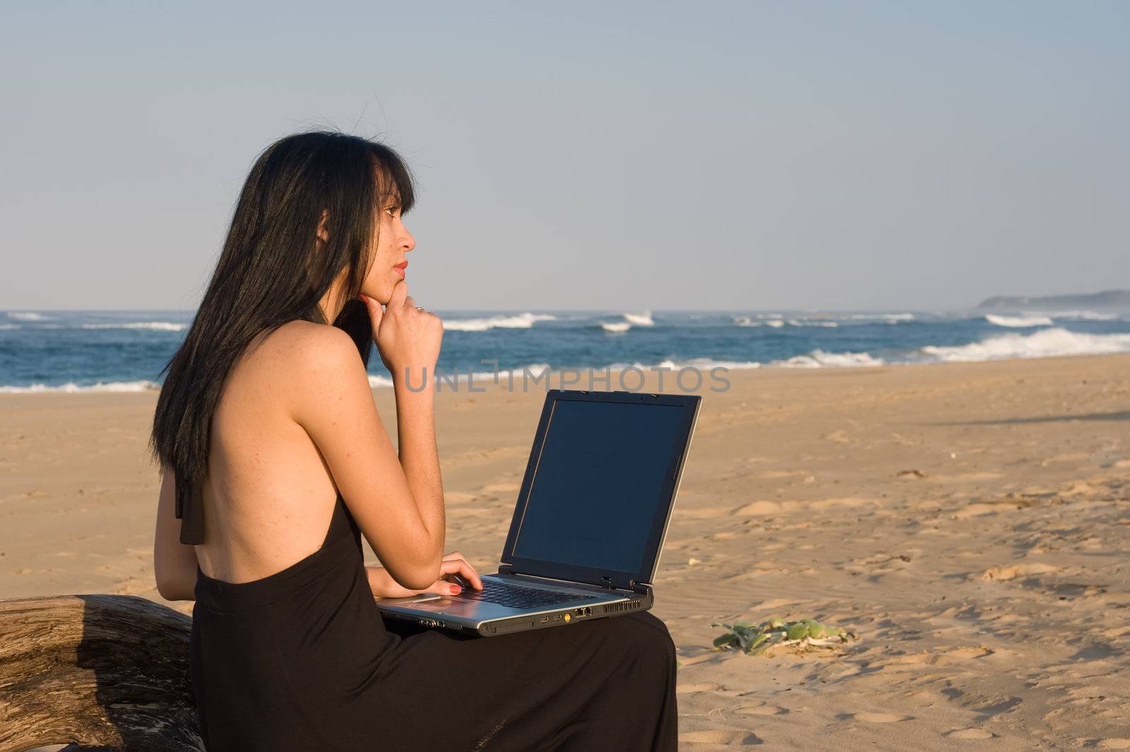 Attractive woman working on a laptop with the beach as background