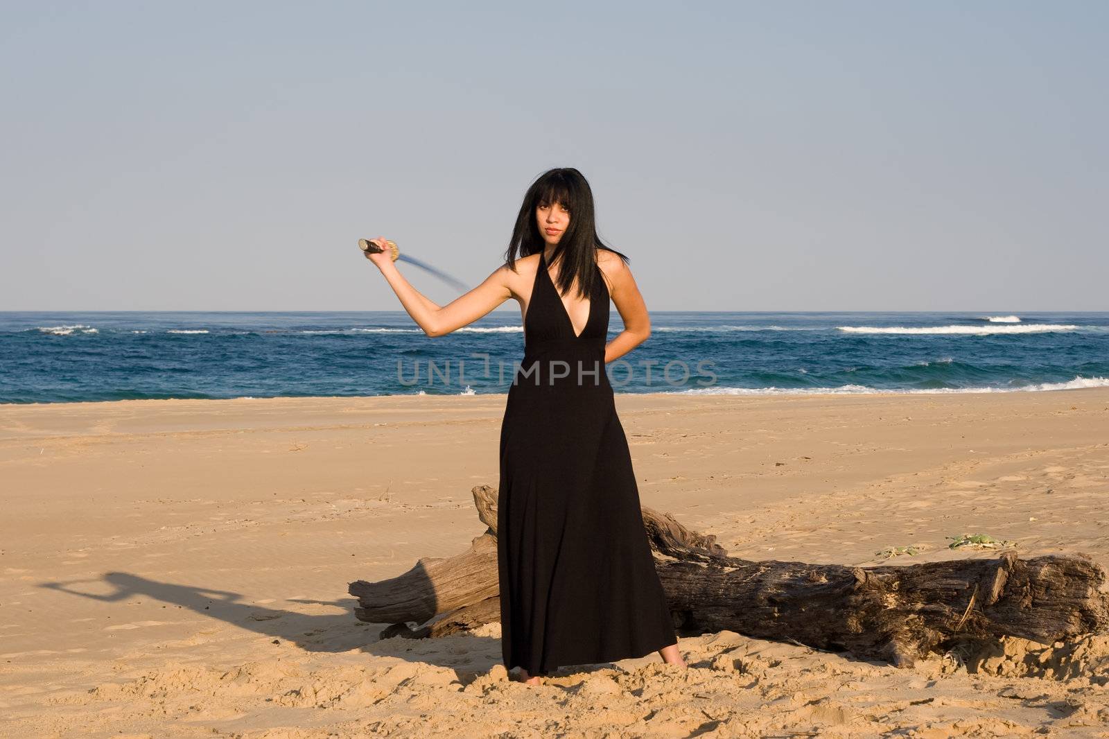 Asian model swinging a sword at the beach