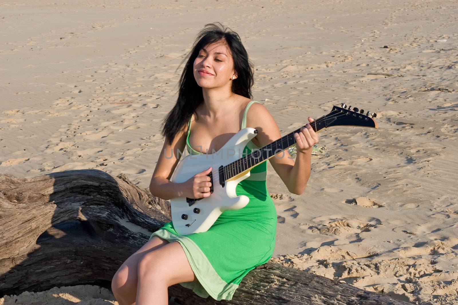 Girl in green dress playing a guitar at the beach