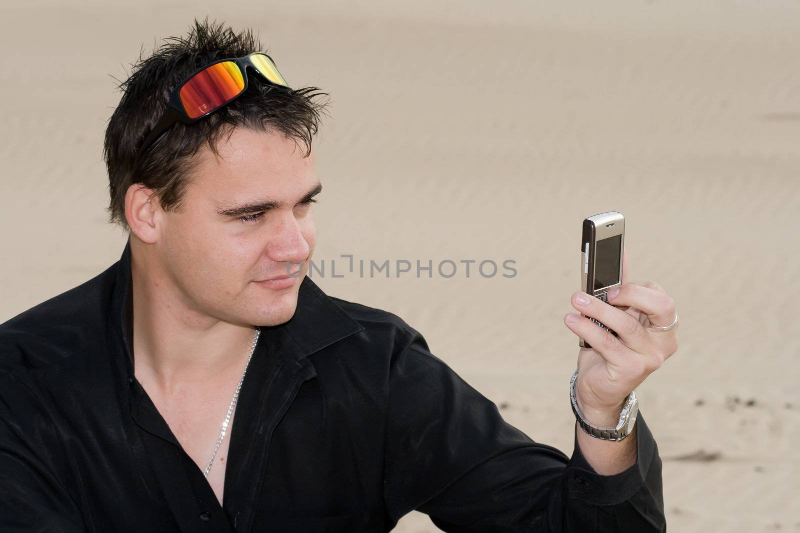 Handsome male model taking a photo of himself with a cellphone camera on the beach