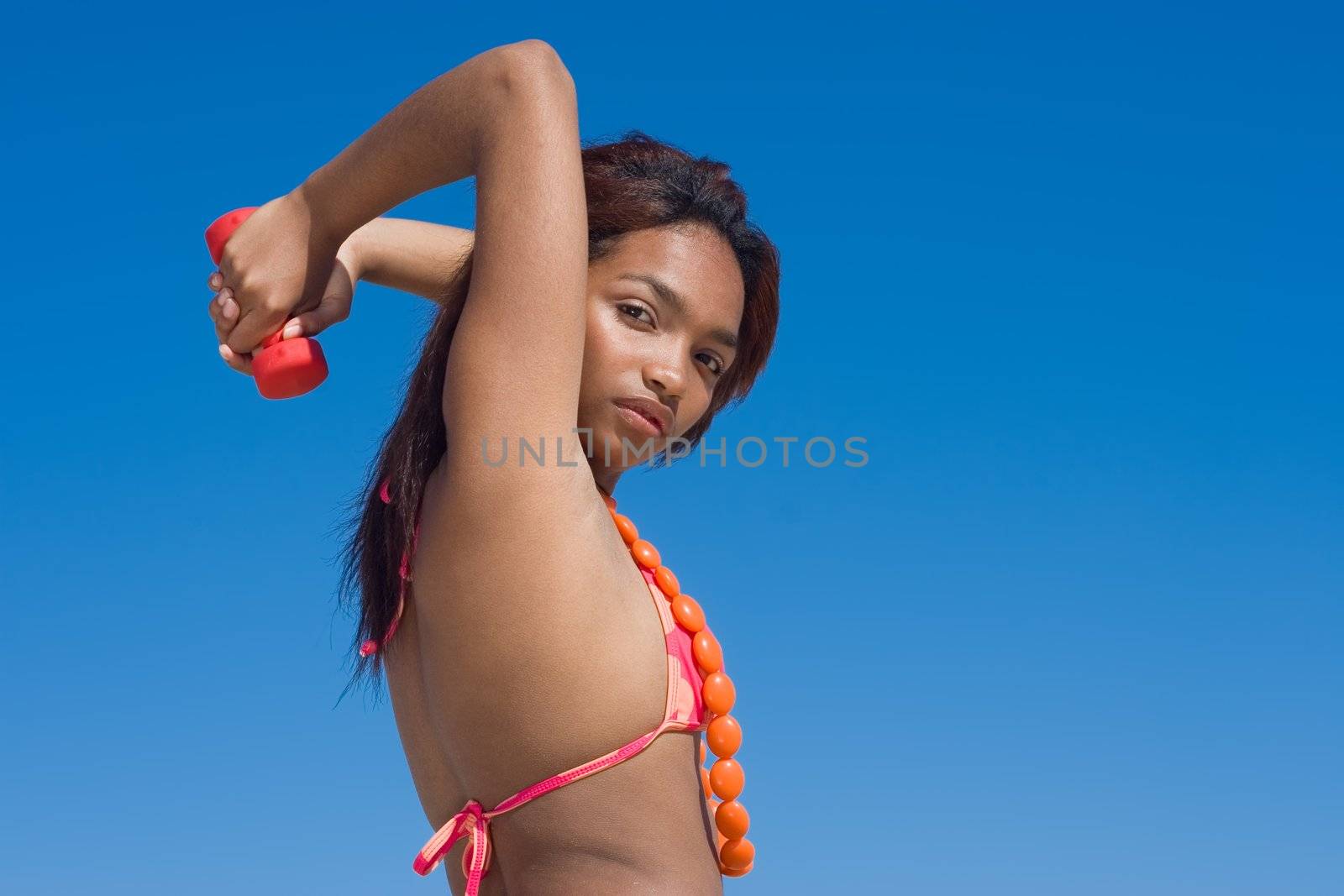 Model with dumbbell exercising with blue sky background.
