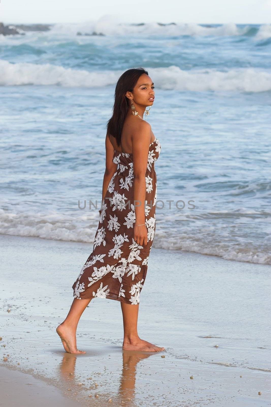 Ethnic model standing on the wet reflective sand at the beach