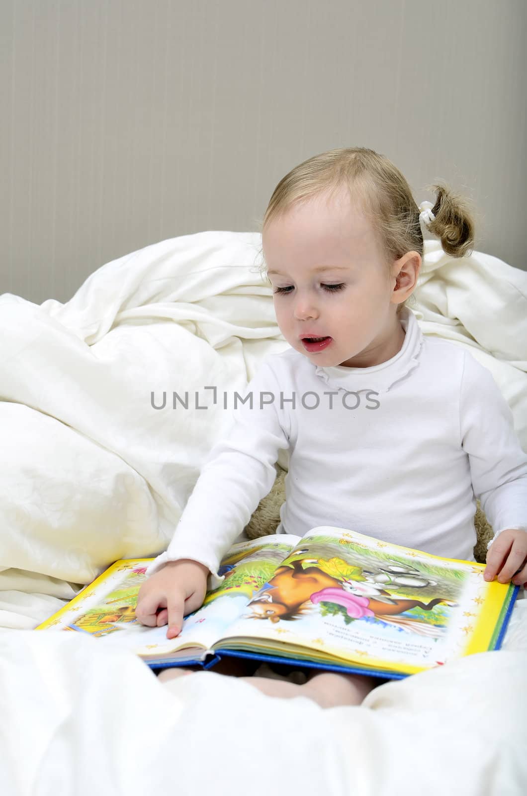 little girl sitting on the bed and reading a book by dmitrimaruta
