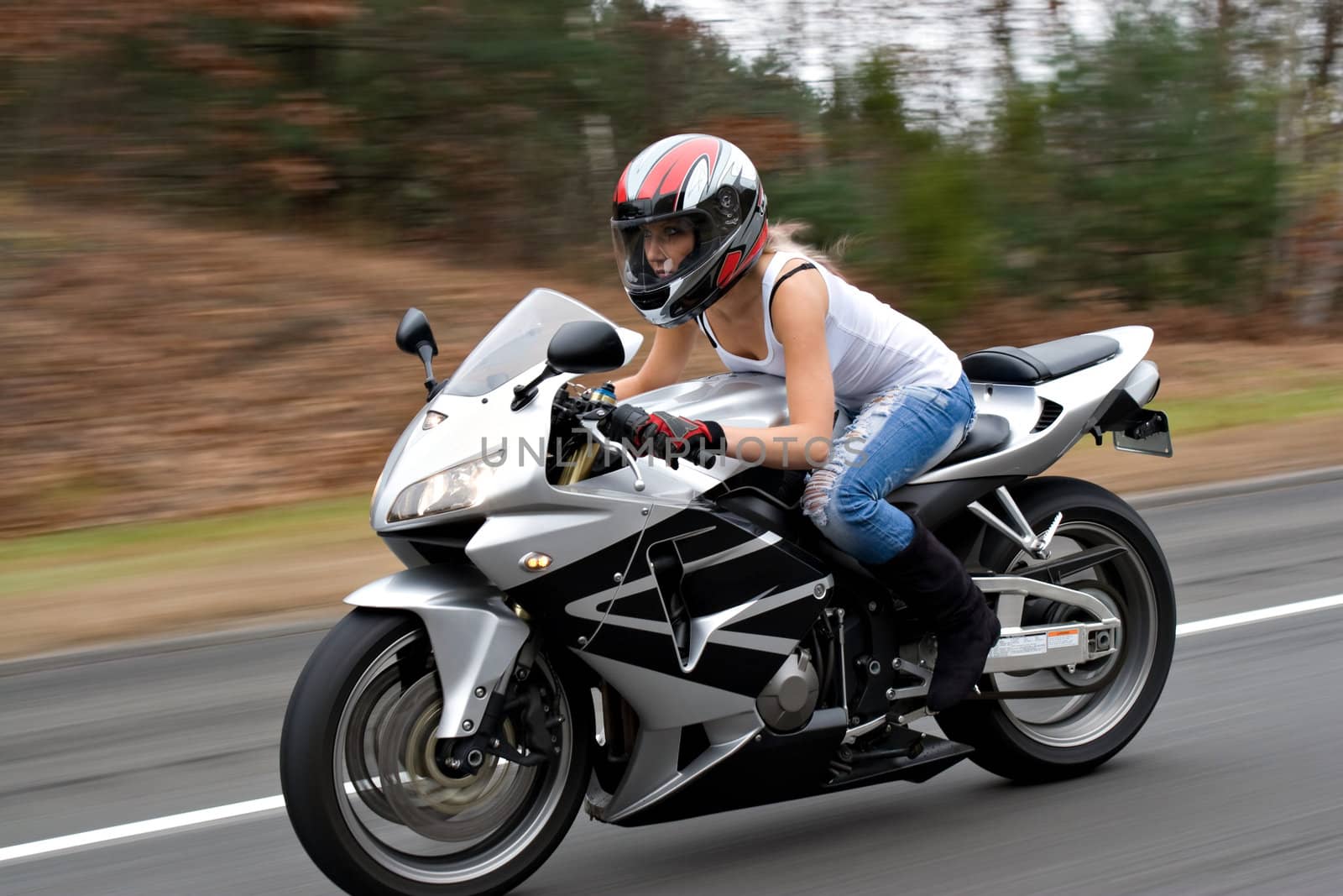 A woman drives a motorcycle at highway speeds with motion blur visible in the background.