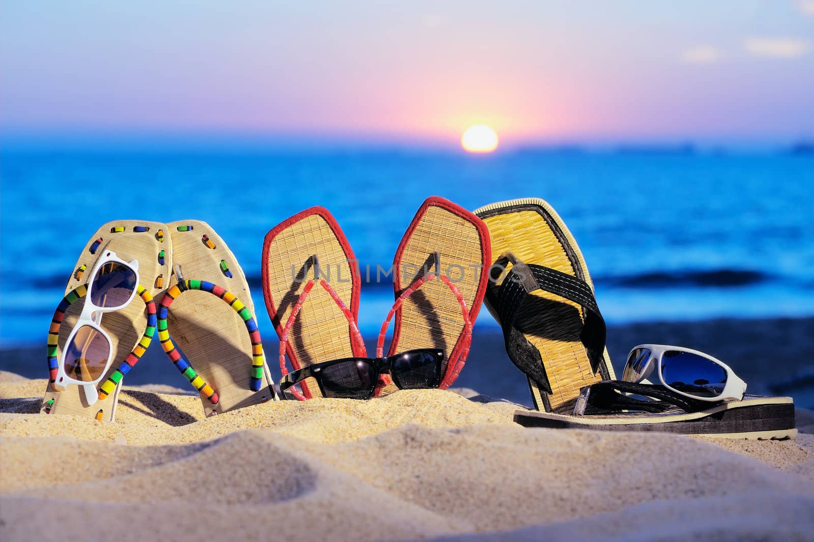 Three pair of beach sandals and glasses on the sandy beach