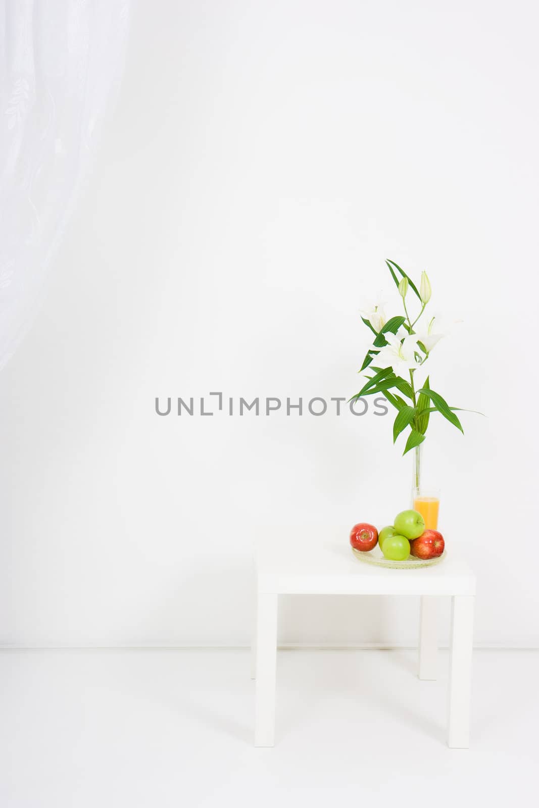 apples, a glass of juice and lilies on the table in a bright room