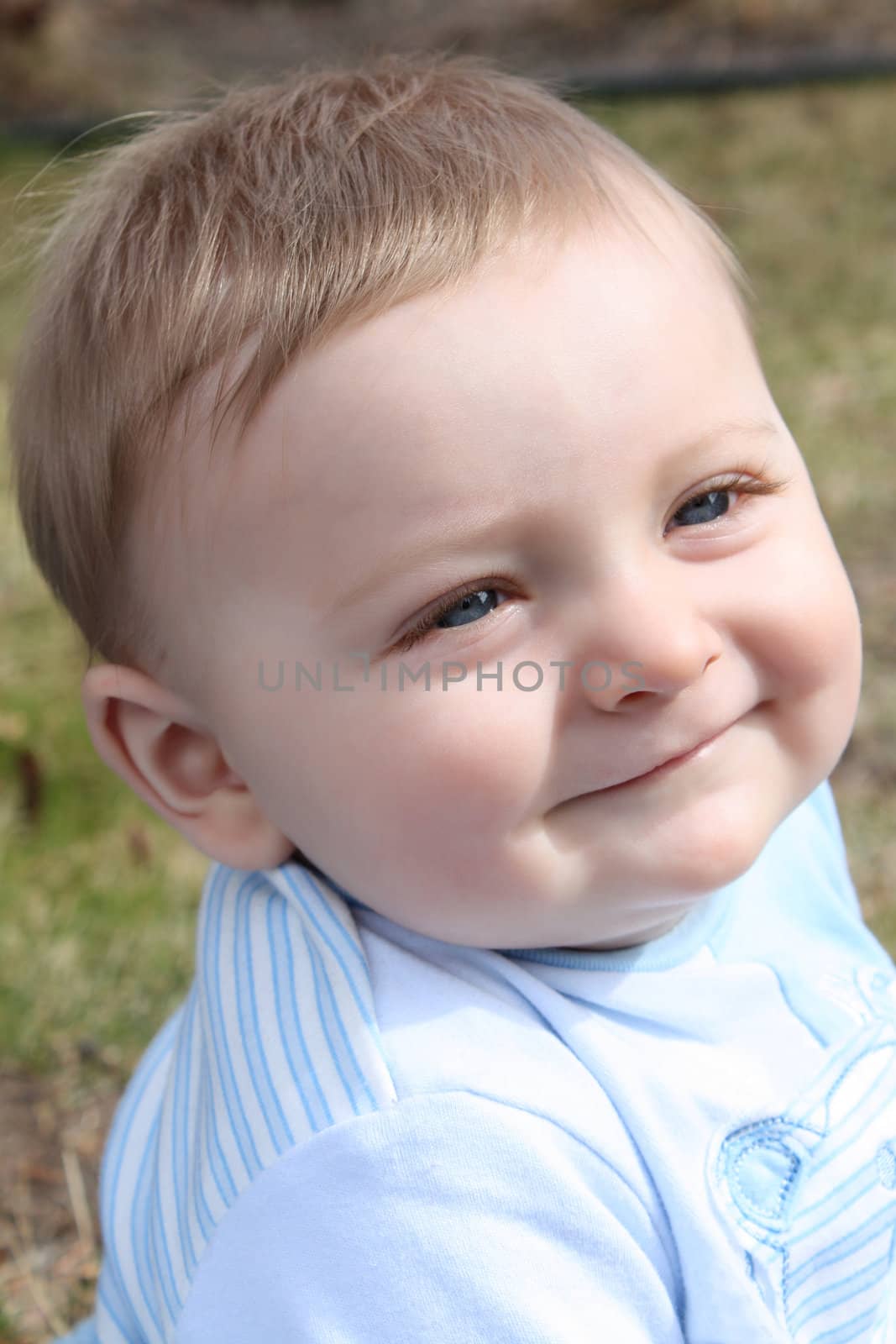 Adorable baby boy sitting outside in the sunny garden 