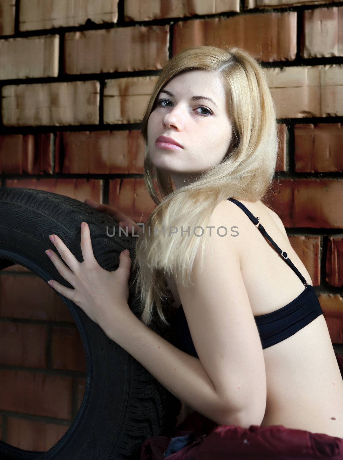 Sexy blonde with a car tire on the background of a brick wall.