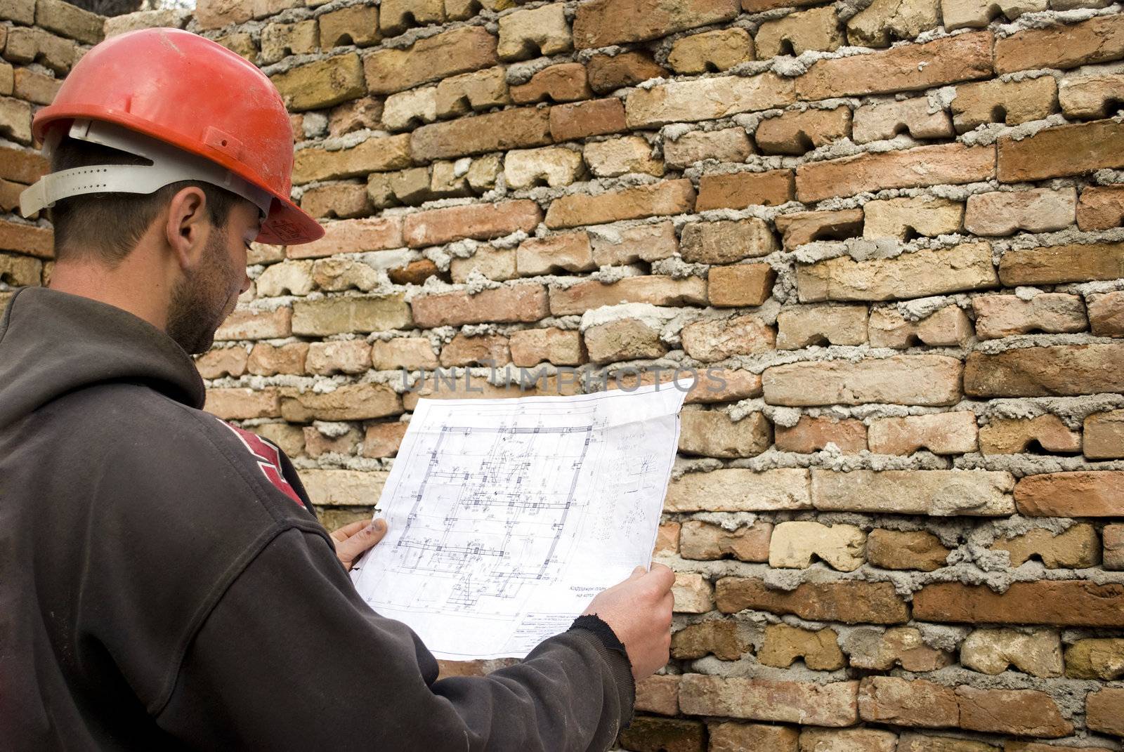 young male builder holding engineer project in front of brick wall