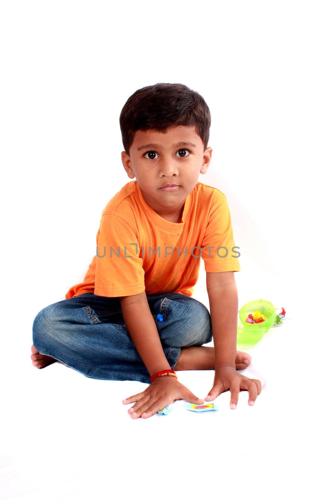 A cute Indian boy sitting on the floor, on white studio background.