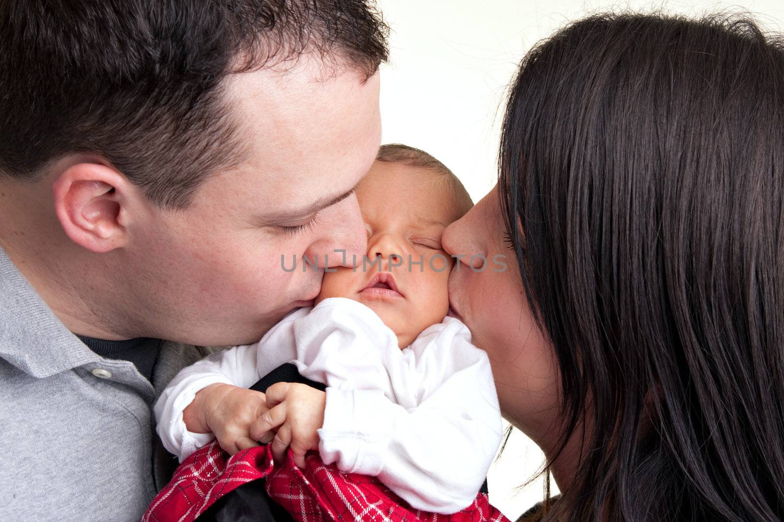 A newborn baby is held by her mother and father as they kiss her cheeks.