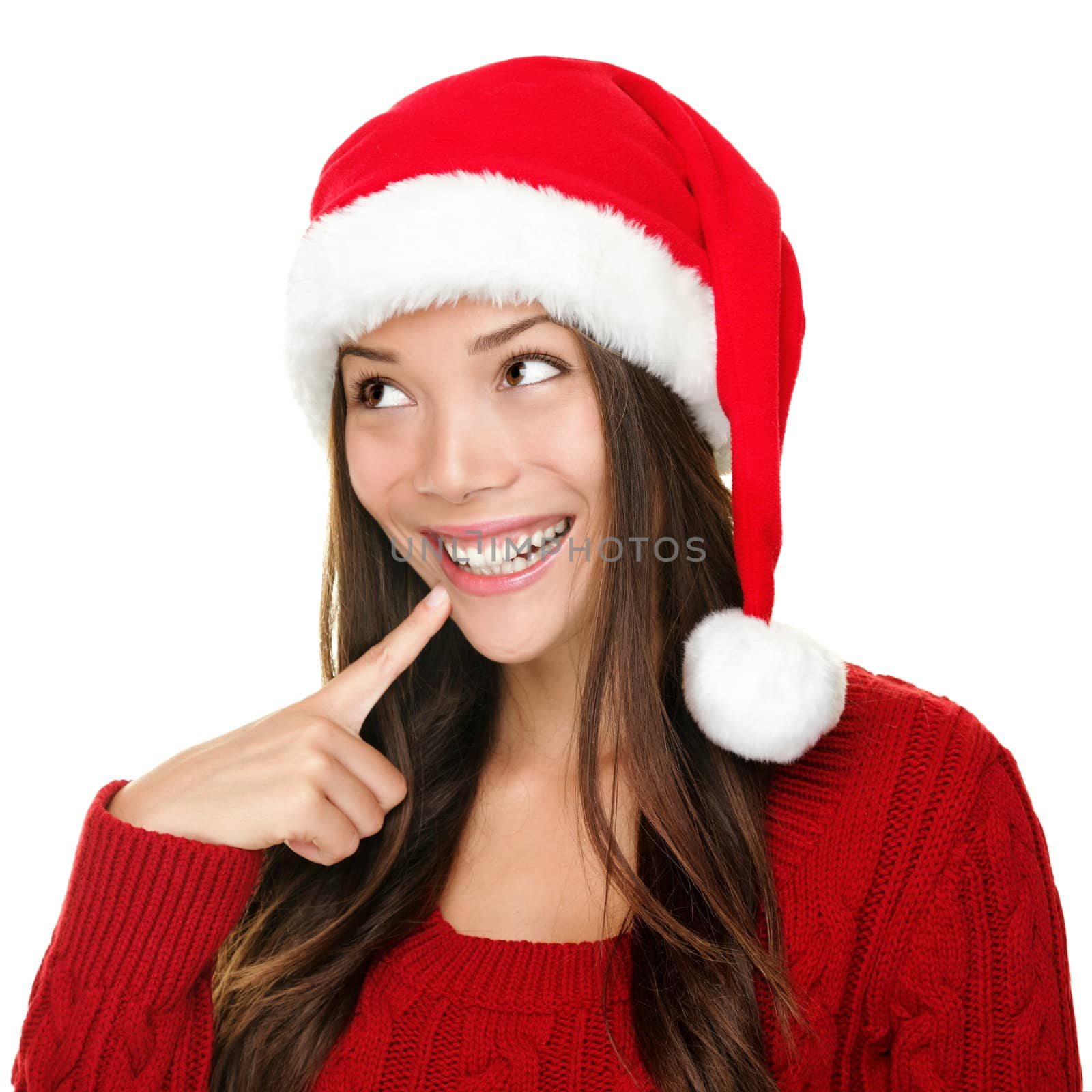 santa christmas woman looking to the side thinking happy and playful. Asian christmas girl wearing santa hat and red sweater isolated on white background.