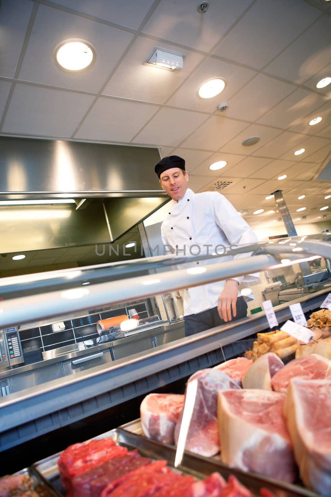 A butcher looking at a fresh meat counter in a grocery store