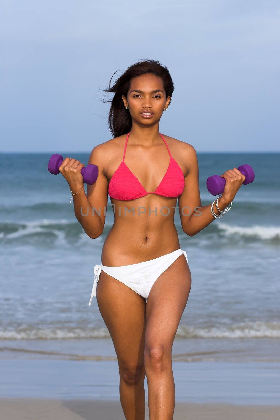 Ethnic Fitness model in bikini with dumbbells in her hands