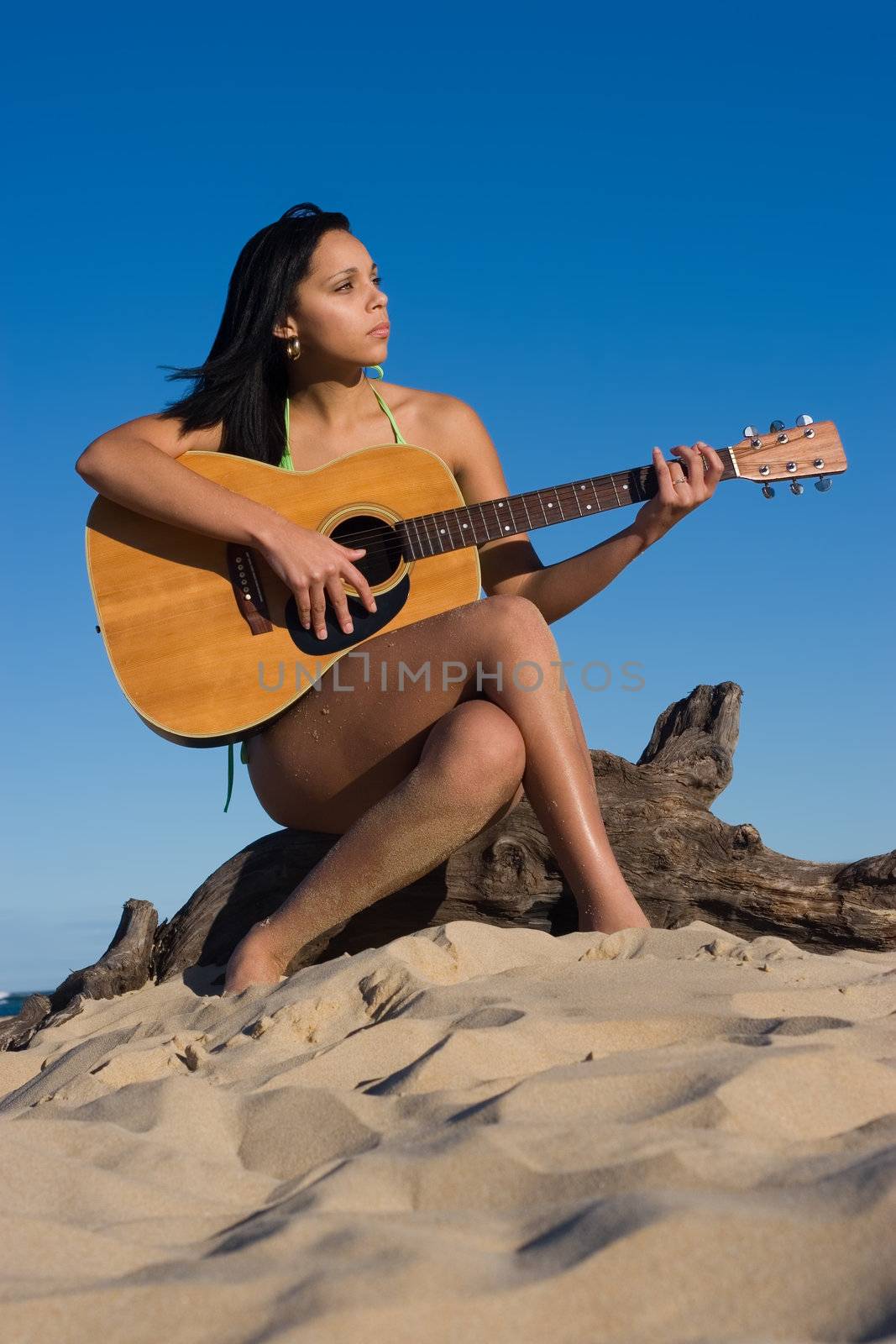 Girl sitting on a log playing a guitar at the beach
