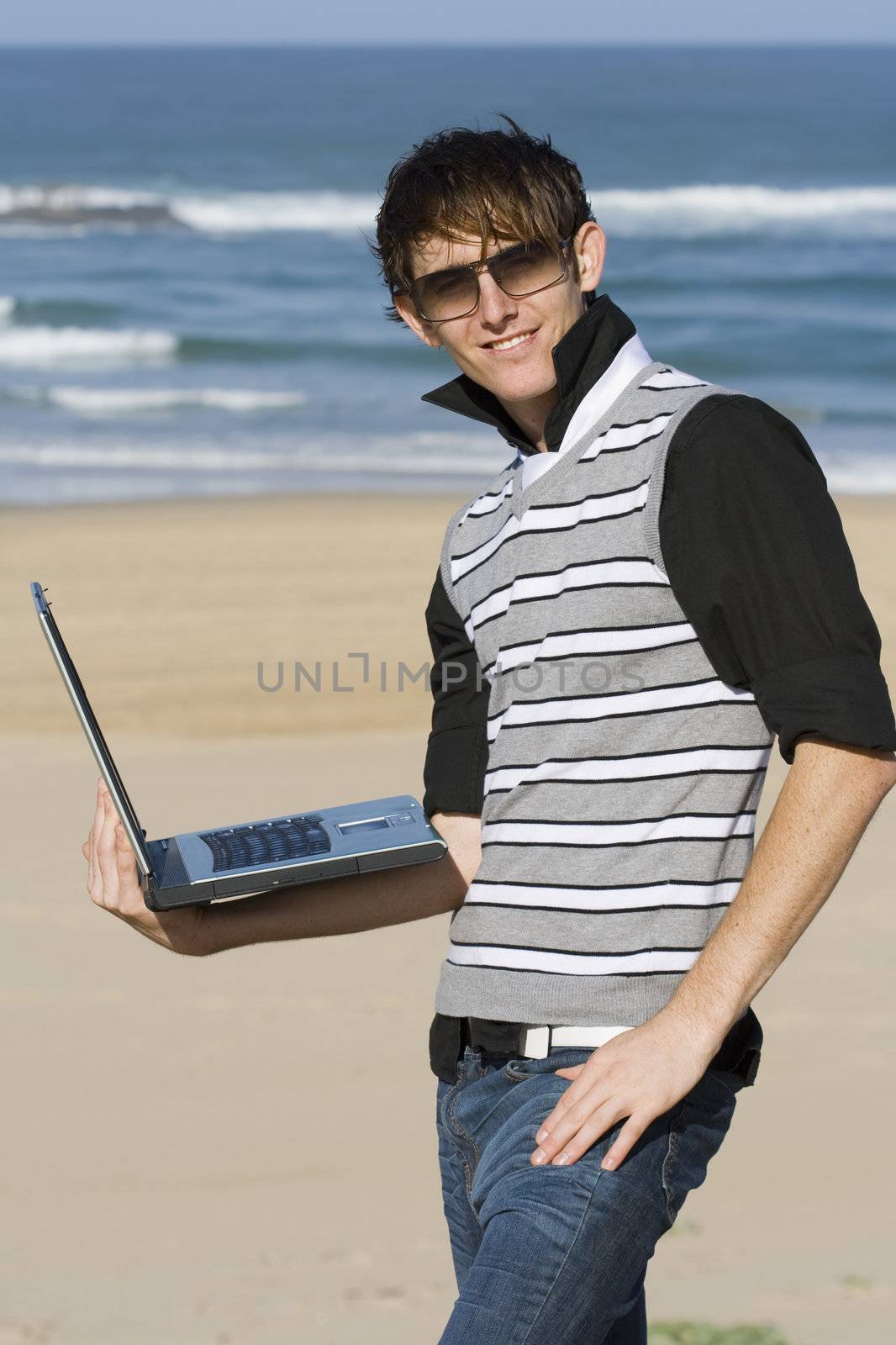 Young professional male standing with laptop at the beach