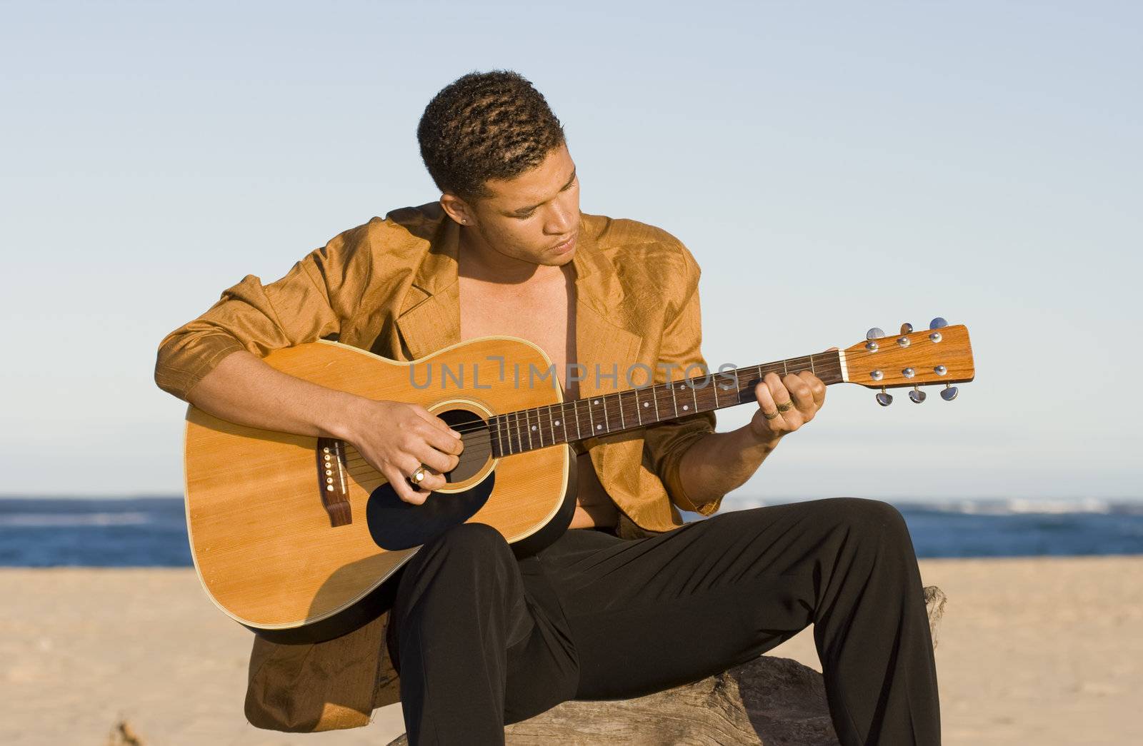 Young man playing his guitar on the beach