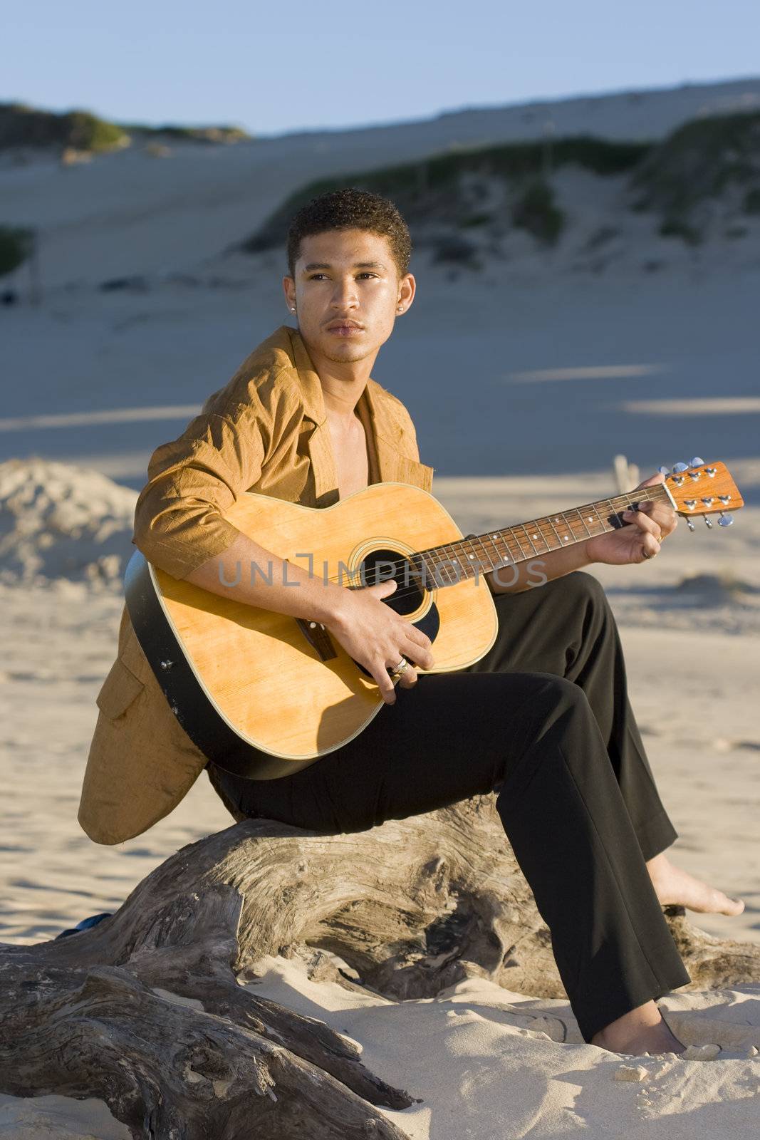 Young man playing his guitar on the beach