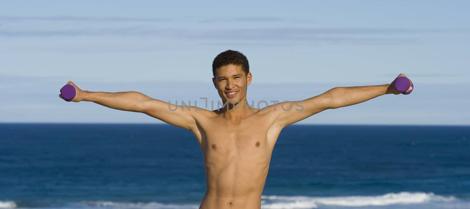 Young fit male, exercising with dumbbells on the beach