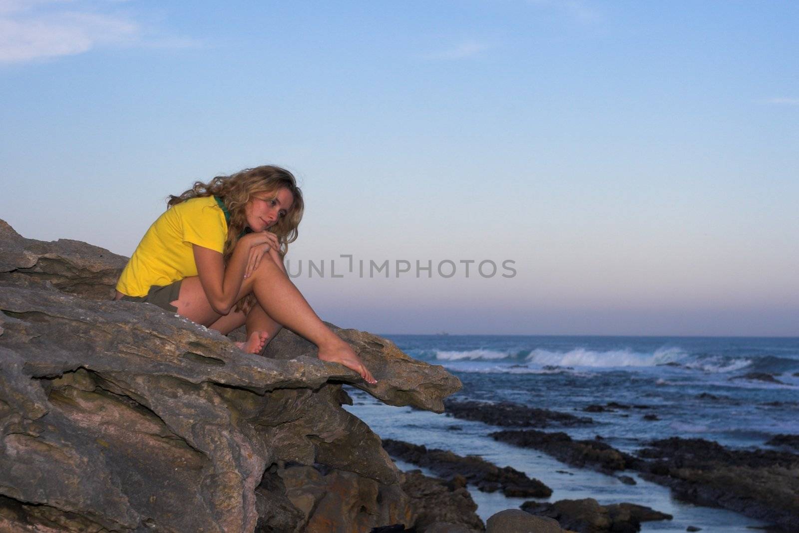 Lonely attractive girl sitting on a rock at the beach