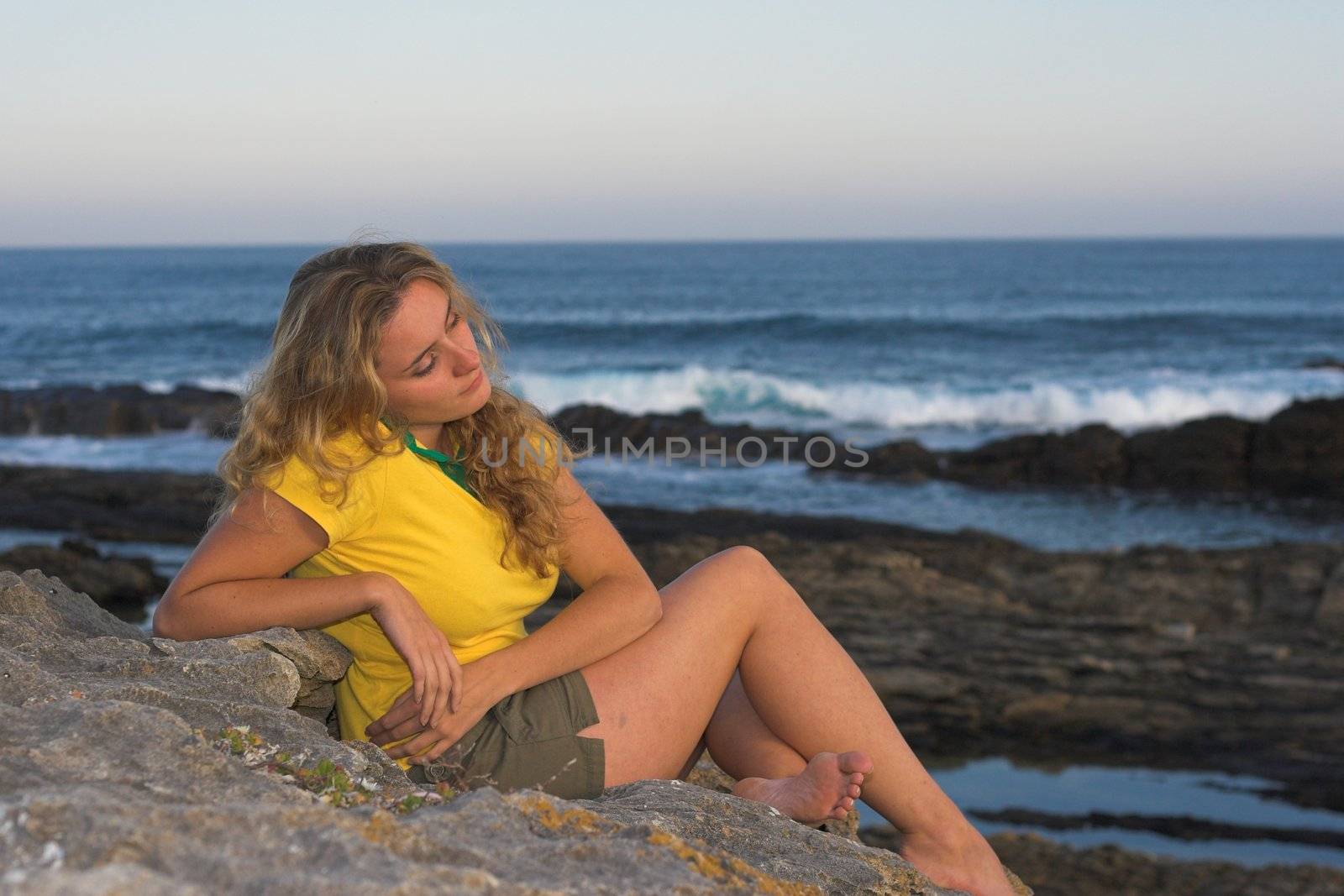 Dreaming girl sitting on a rock at the beach