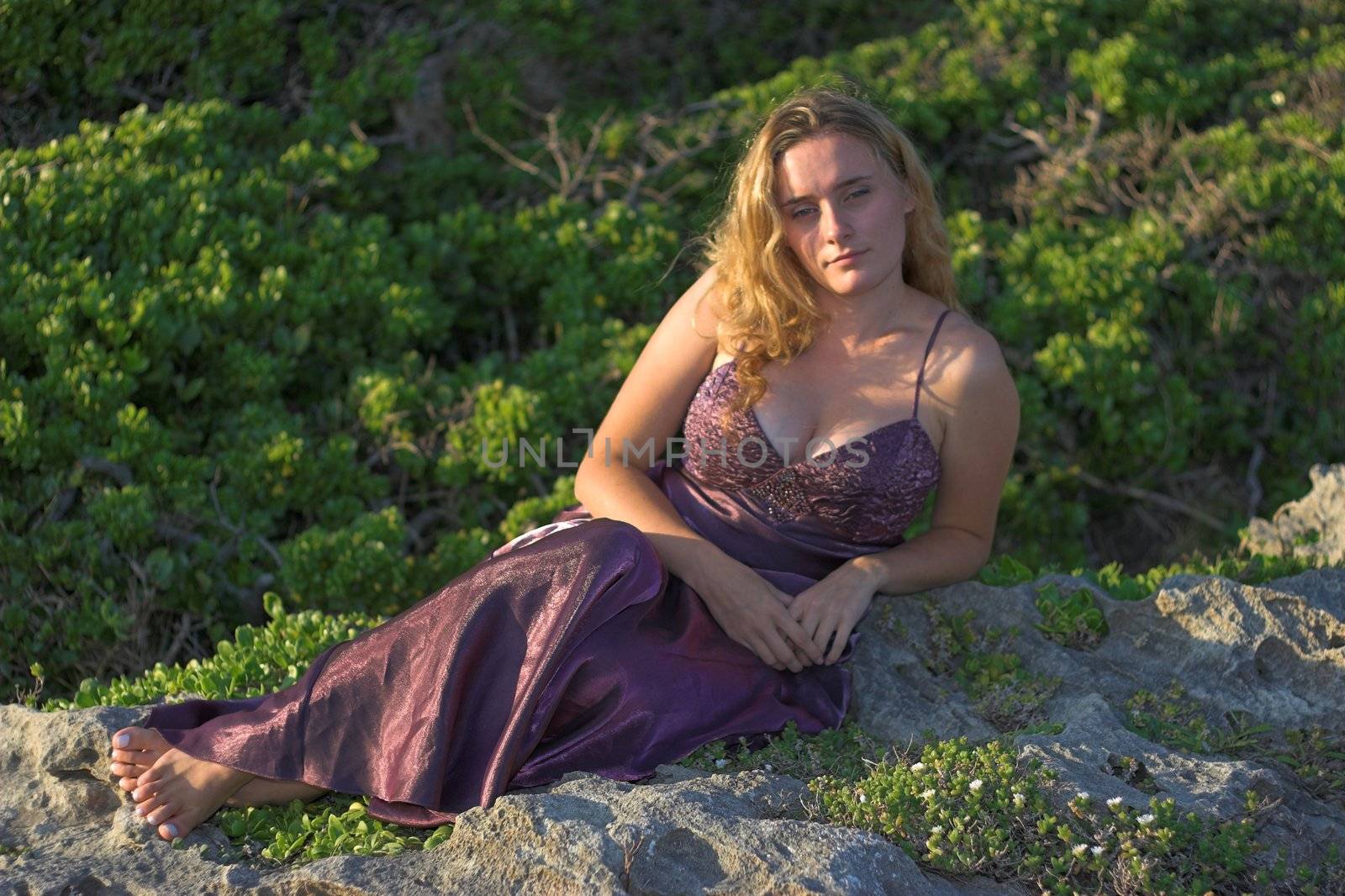Attractive girl in evening dress sitting on a rock