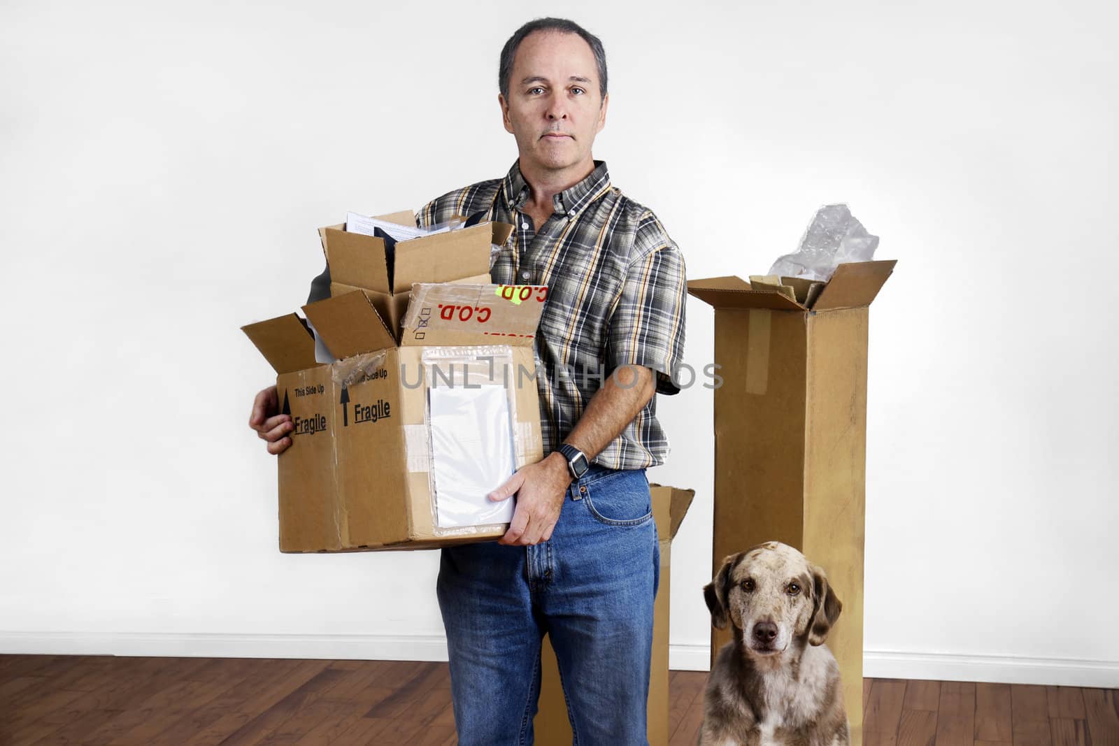 MIddle age man and dog moving out holding boxes looking sad in empty bare room.