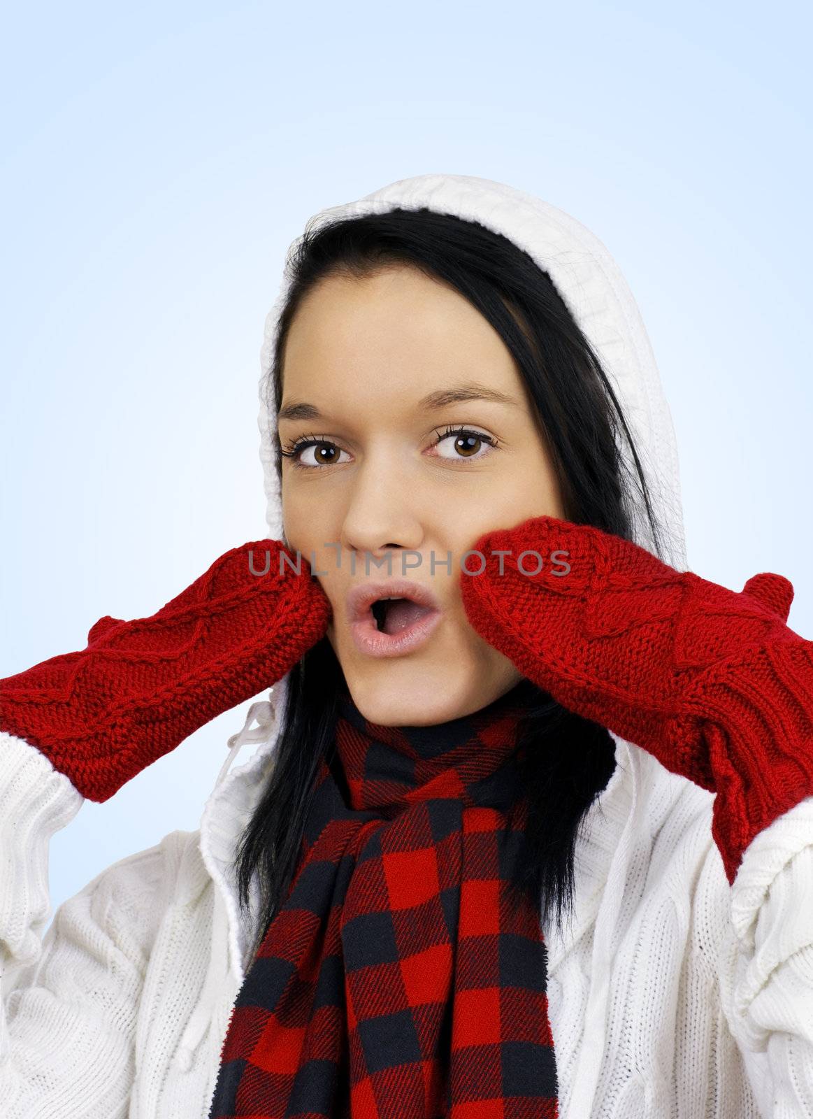 Winter time concept: cute oh my it's cold friendly natural young woman with red mittens and white hoodie over light blue background.