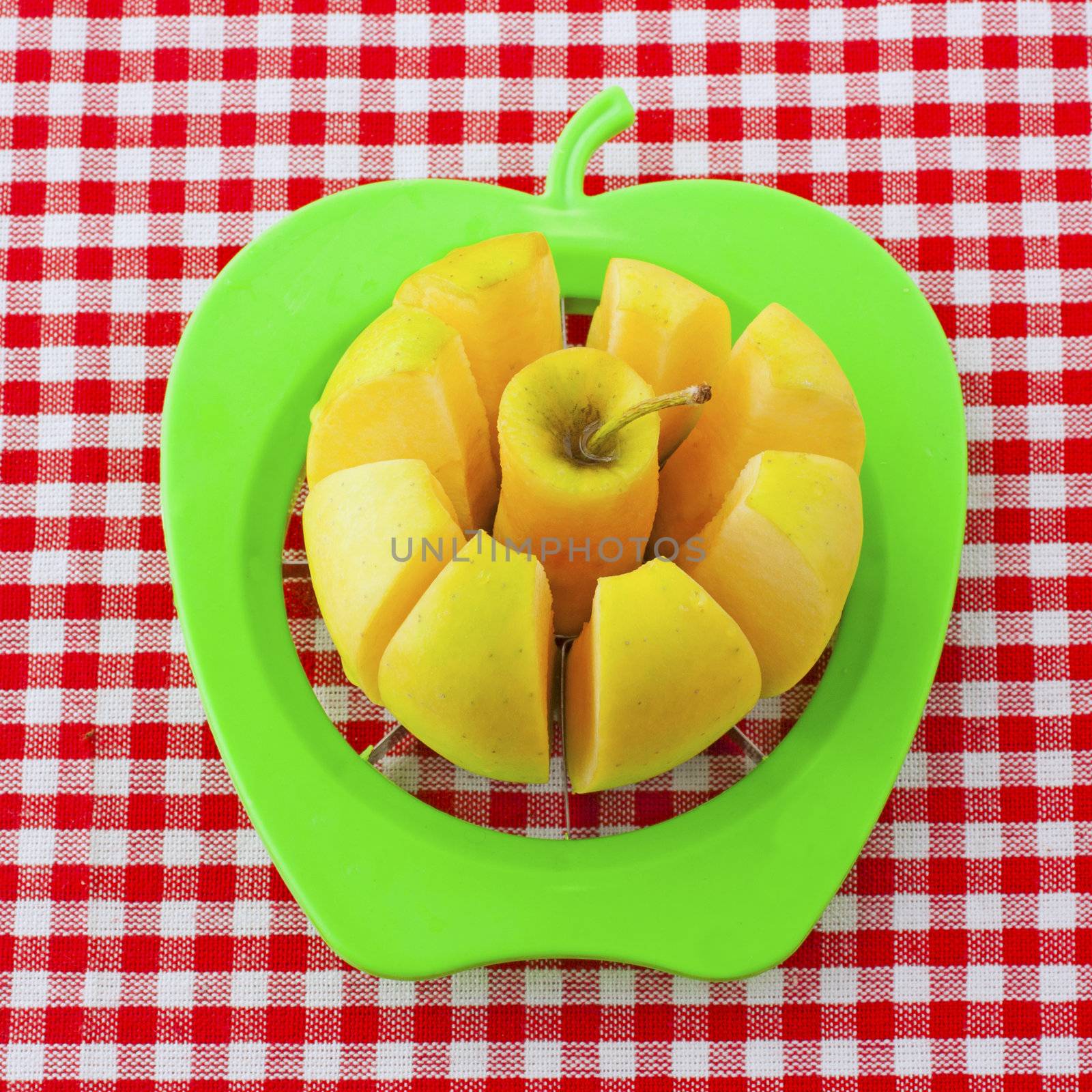 Yellow apple cut by a green tool over white and red cloth