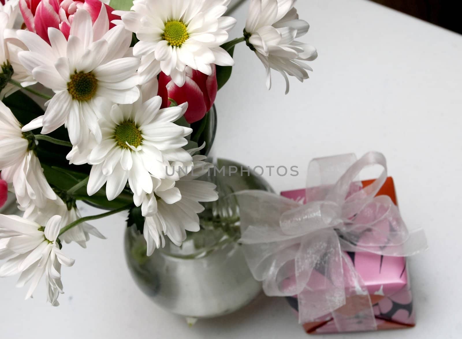 a bouquet of daisies and other spring flowers and a small gift