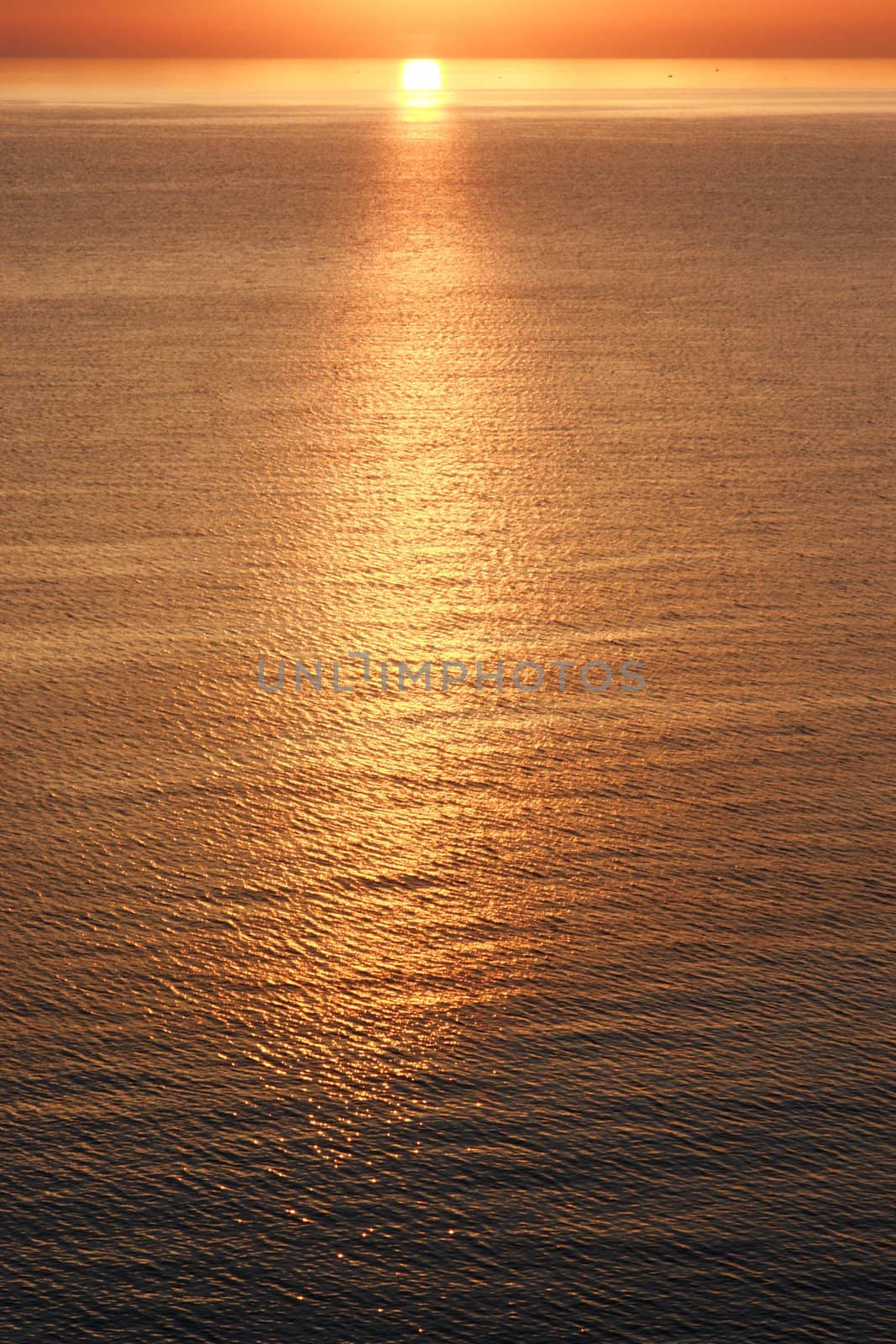 A view from the beach with a yellow glowing sun setting in the horizon. The picture has a warm glow and the sun is reflecting from the water.